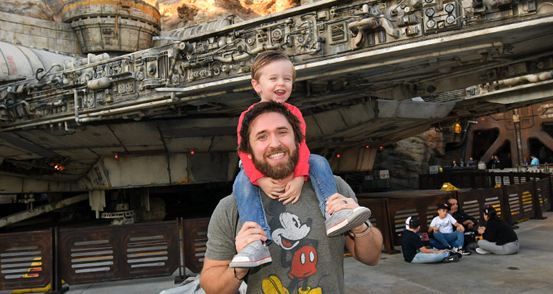 employee chad smiling with son at disney world in front of millenium falcon